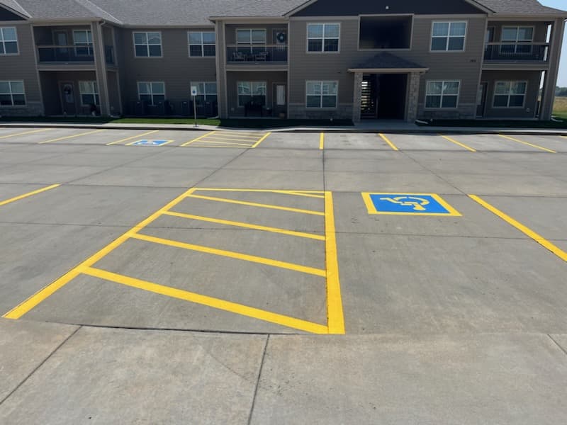A blue accessible parking symbol and yellow diagonal hatching in the access aisle beside it, in front of an apartment building.