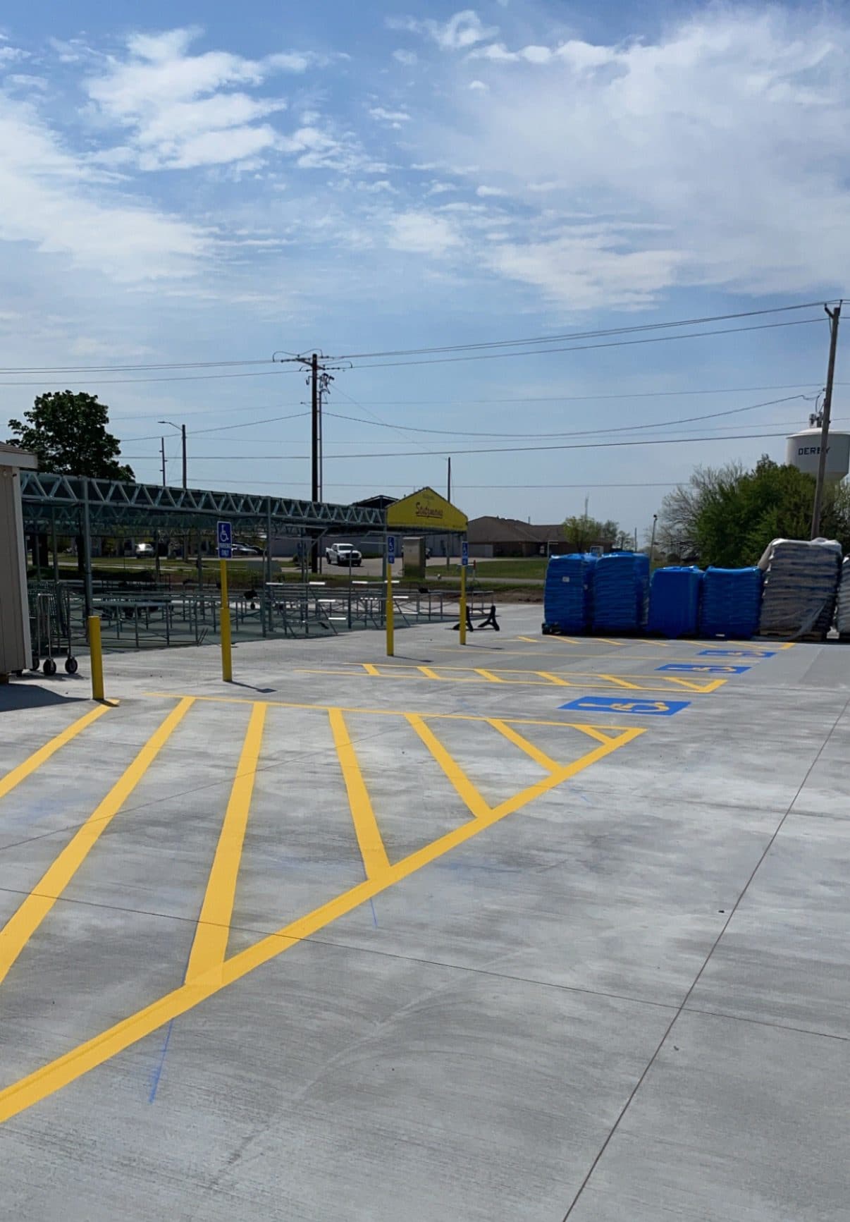 New yellow hatched access aisles and blue accessible stall symbols on fresh concrete, with yellow bollards and accessible parking signs along the edge.