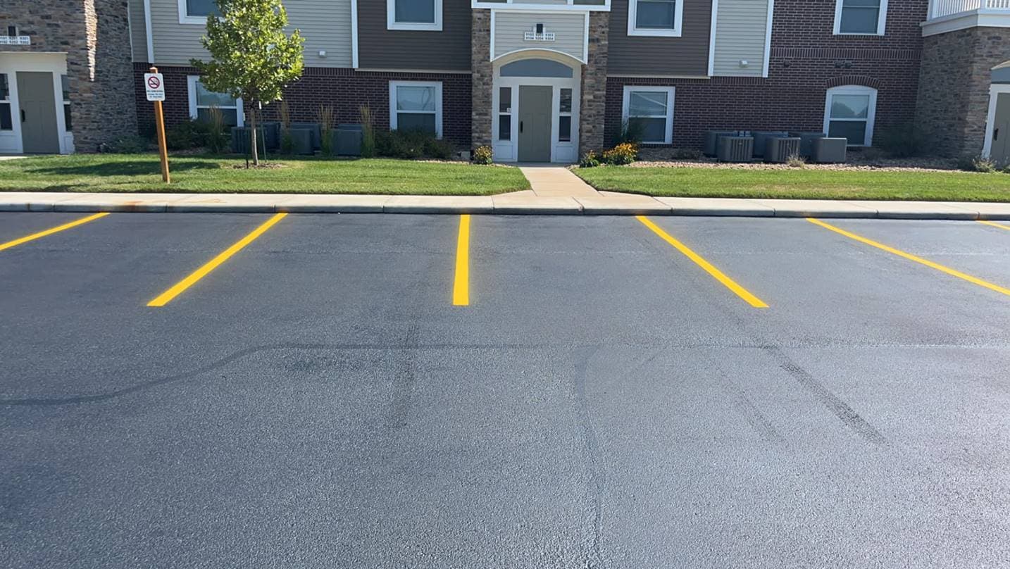Freshly painted double yellow stall lines in an apartment complex parking lot, with the front entrance and landscaped beds visible.