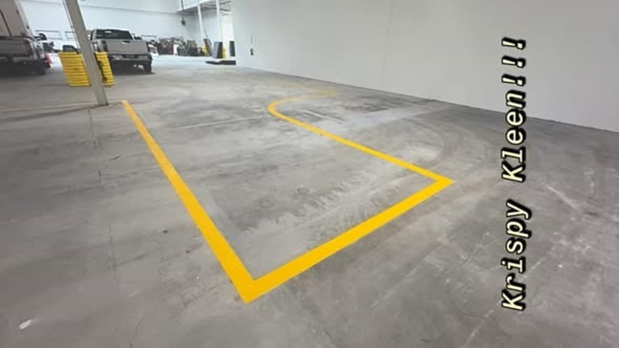 A wide interior warehouse view with yellow floor striping marking a work zone, tall support columns and roll-up doors along the far wall.