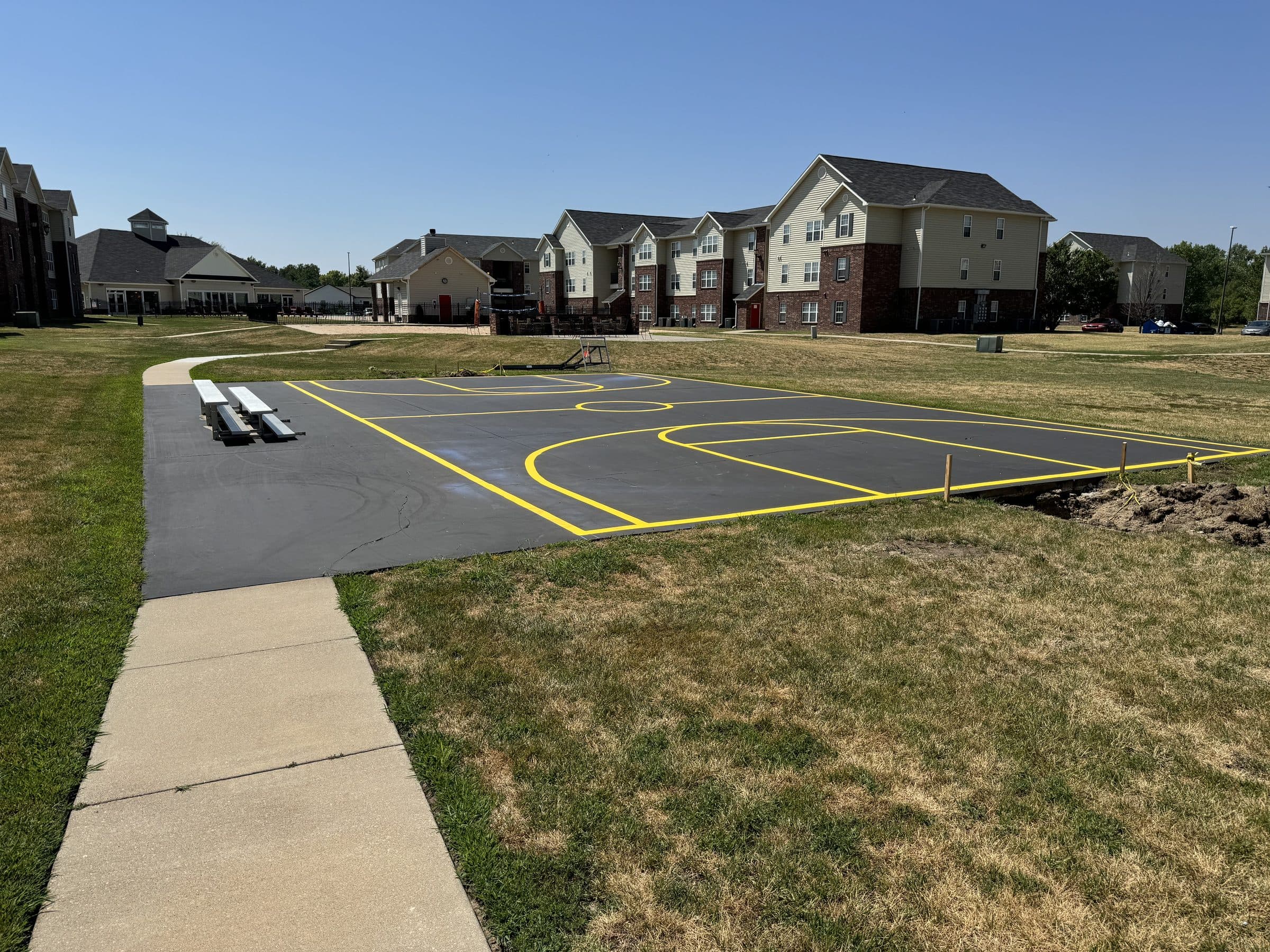 A freshly coated outdoor basketball court with bright yellow court lines, set in the lawn of an apartment community.