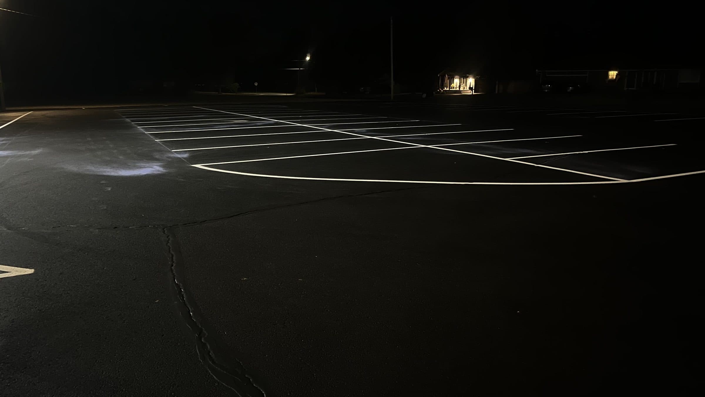 A freshly striped parking lot at night with crisp white stall lines and a long filled crack running through the asphalt in the foreground.
