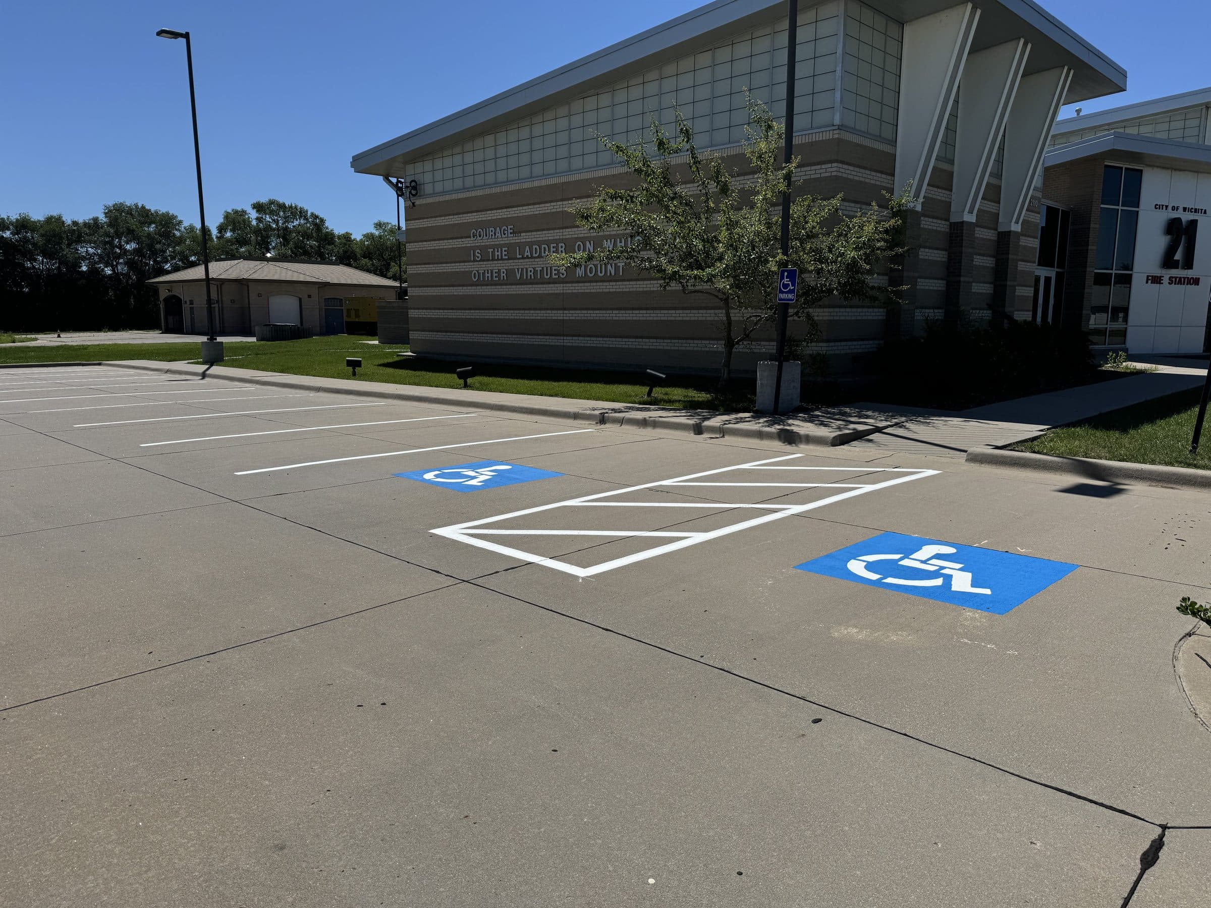 Two blue accessible parking stalls with a shared white hatched access aisle in front of a public building.