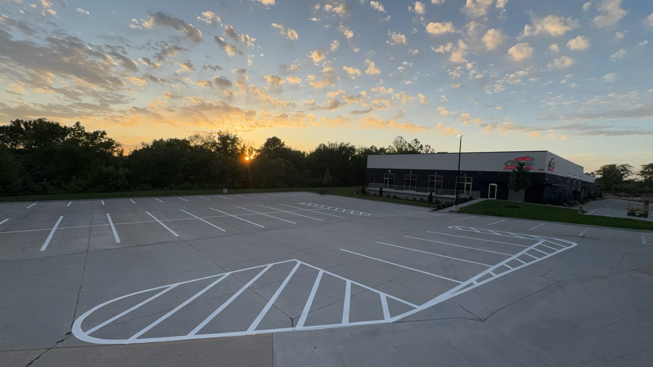 A newly striped concrete lot at sunset with white stall lines and two large white cross hatched islands curving across the pavement.