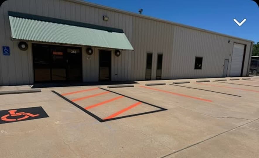 Orange and black striped loading zone markings on a warehouse dock apron, with an accessible stall marked on the pavement to the left.