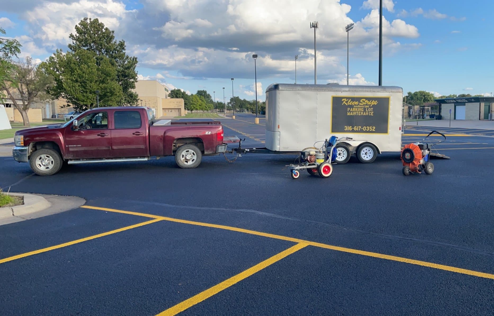 The Kleen Stripe pickup and enclosed trailer parked on a freshly striped lot, with a line striper and a walk behind blower set out beside the trailer.